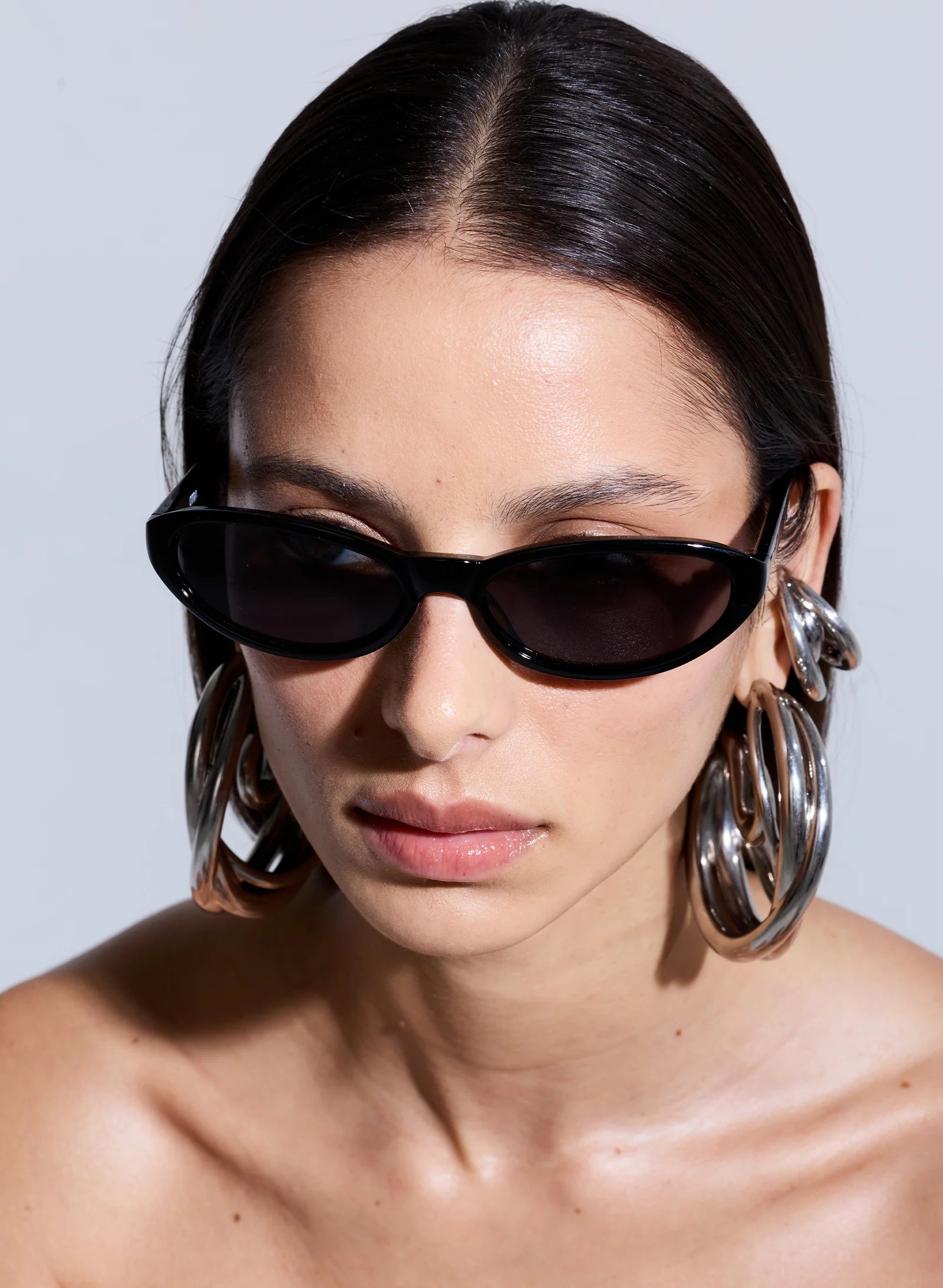 Woman wearing large hoop earrings and sunglasses against a plain background