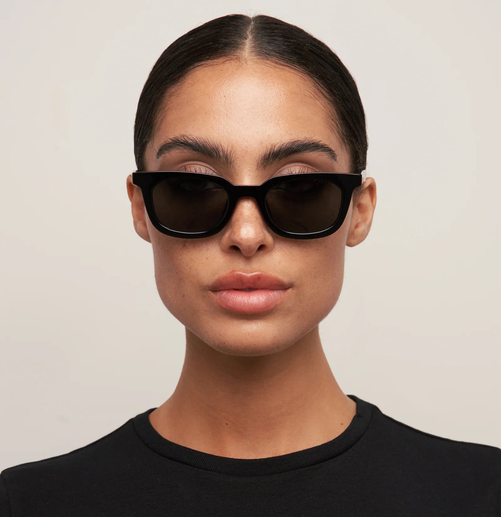 Person wearing black sunglasses and a black shirt against a plain background
