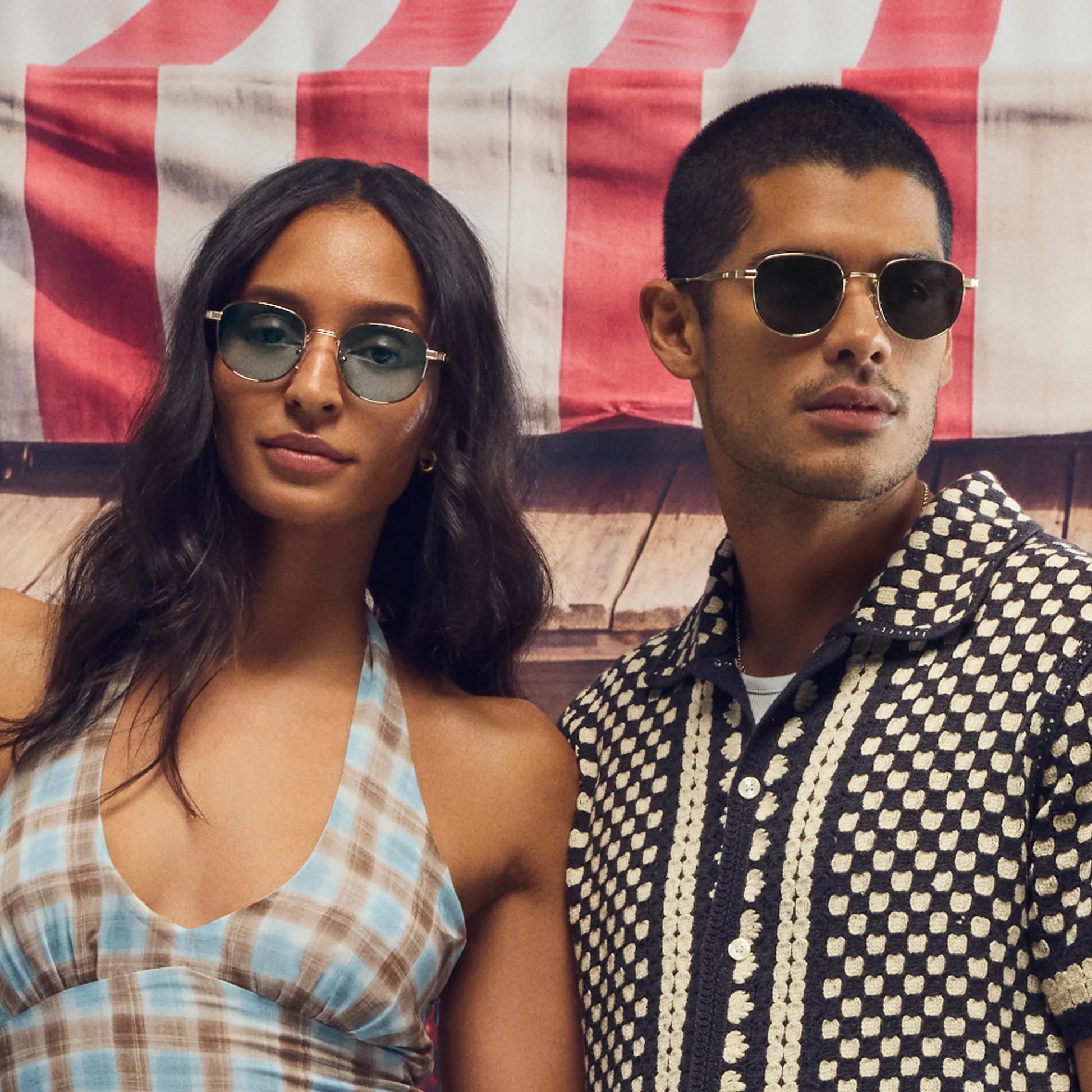 Two people wearing sunglasses in front of an American flag.