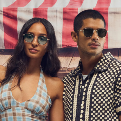 Two people wearing sunglasses in front of an American flag.