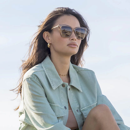 Woman wearing sunglasses and a light green jacket against a clear blue sky