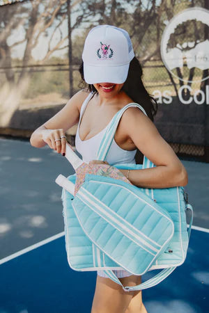 Woman holding a blue pickleball paddle and bag on a tennis court