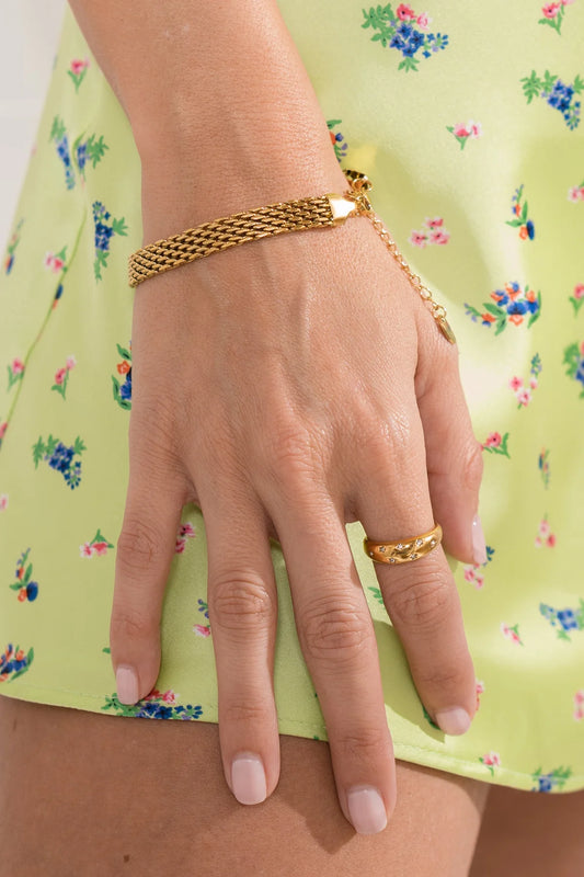 Hand wearing a gold bracelet and ring against a floral background