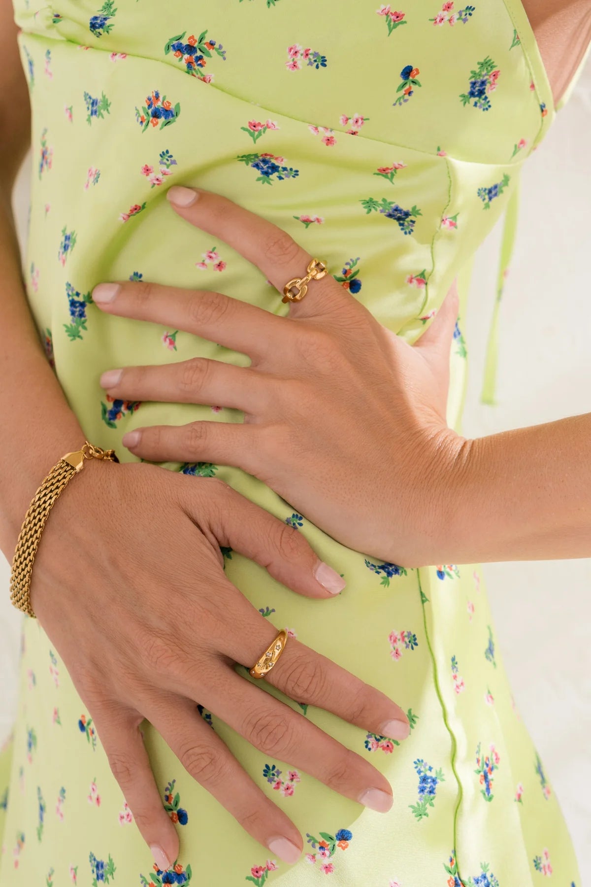 Close-up of hands wearing gold rings on a light green floral dress.