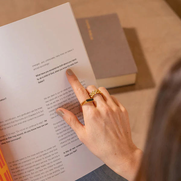 Person reading a book with a gold ring on a wooden surface