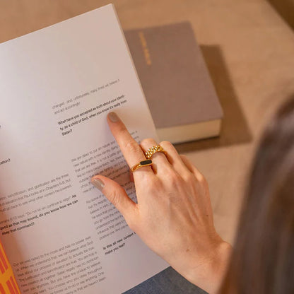 Person reading a book with a gold ring on a wooden surface