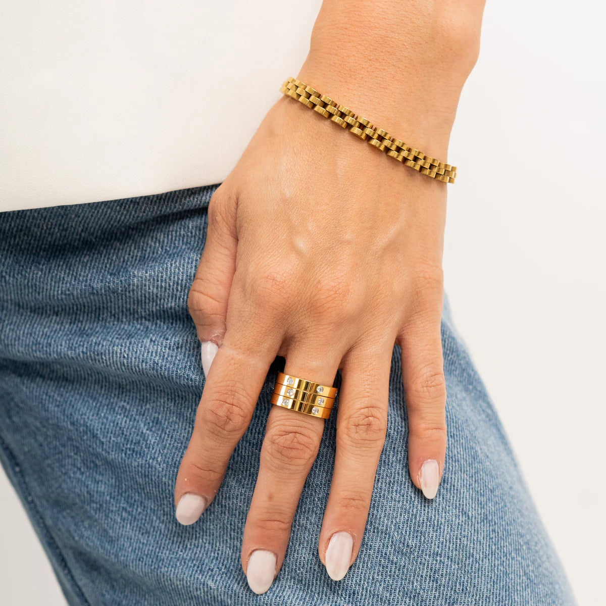 Hand wearing a gold bracelet and ring on a light background