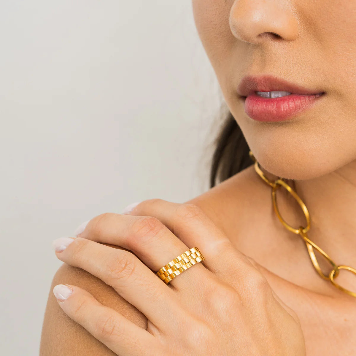 Close-up of a person wearing a gold ring and necklace on a neutral background