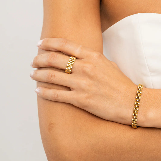 Gold ring and bracelet on a person's wrist against a neutral background