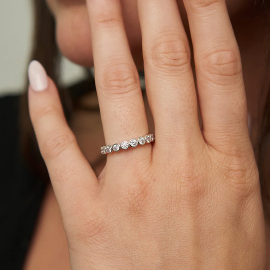 Close-up of a hand wearing a silver ring with small diamonds on a blurred background