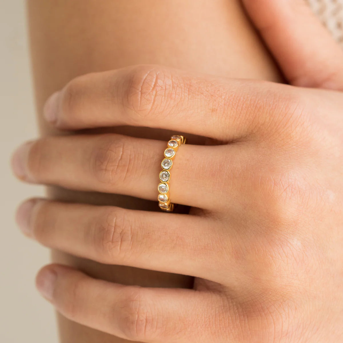 Gold ring with diamonds on a person's finger against a neutral background