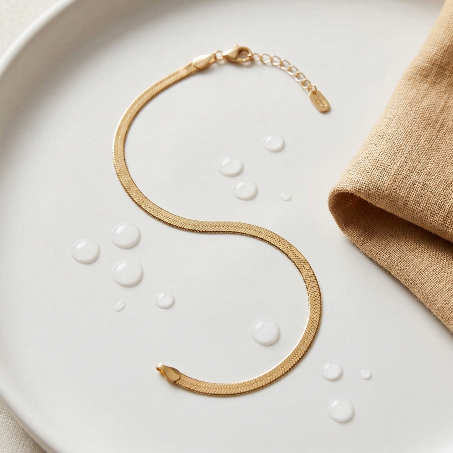 Gold anklet on a white surface with a beige fabric napkin