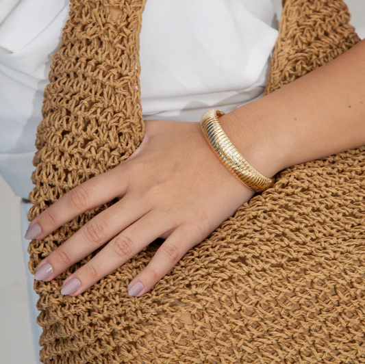 Hand wearing a gold bracelet on a textured brown surface