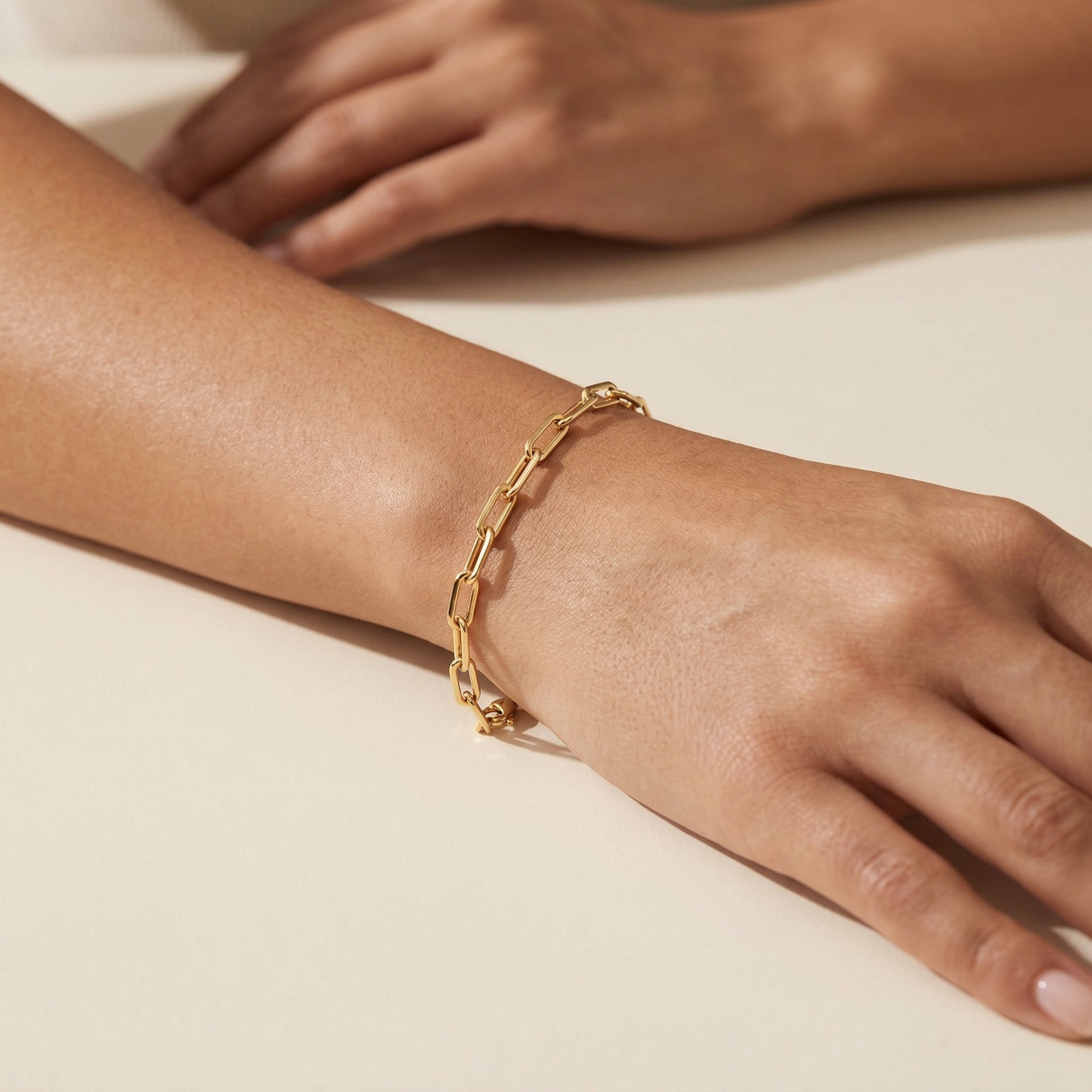 Gold chain bracelet on a wrist with a neutral background