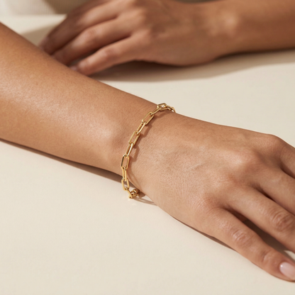 Gold chain bracelet on a wrist with a neutral background