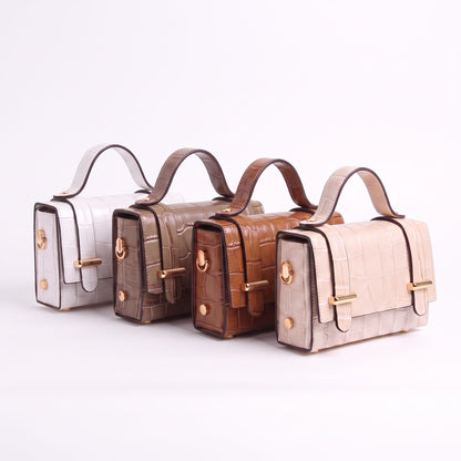 Four structured handbags with crocodile-embossed leather texture, arranged in a row on a light off-white background. The colors of the bags are silver, taupe, medium brown, and light beige, all with gold-tone hardware.